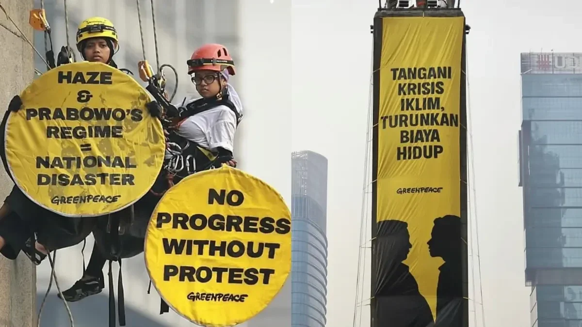 Greenpeace Indonesia activists on rope access gear holding yellow signs, and a yellow banner on the Selamat Datang monument at Bundaran HI, Jakarta